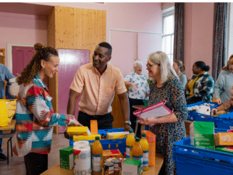 A diverse group of people gathered at a community food bank surrounded by food donations